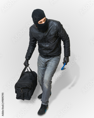 Masked burglar or thief with balaclava is creeping with black balaclava and black bag on white background.