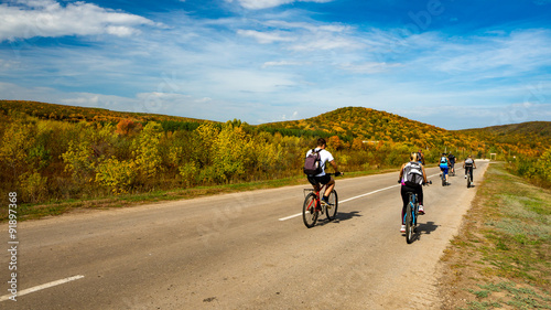 Group of cyclists on road stretches into the distance on the background of bright autumn trees on a hill. Russia