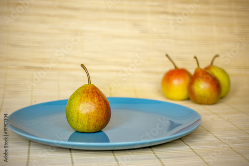 one ripe pear on a blue plate with several in the background