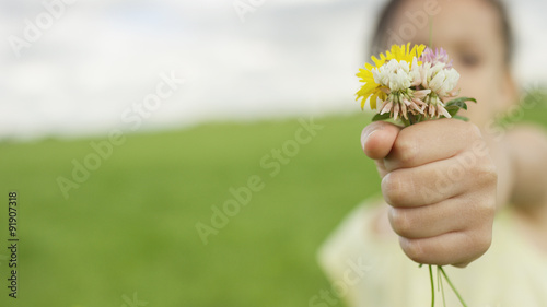 Foreground focus of a bunch of hand picked flowers offered by a child blurred in the background