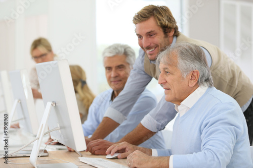 Instructor helping senior men with computing class © goodluz