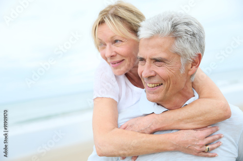 Senior man giving piggyback ride to his wife on the beach