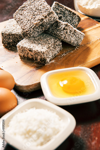 Group of Lamingtons on a timber cutting board with food ingredients in the backgrou