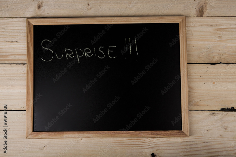 Lavagna con scritta surprise su sfondo di legno