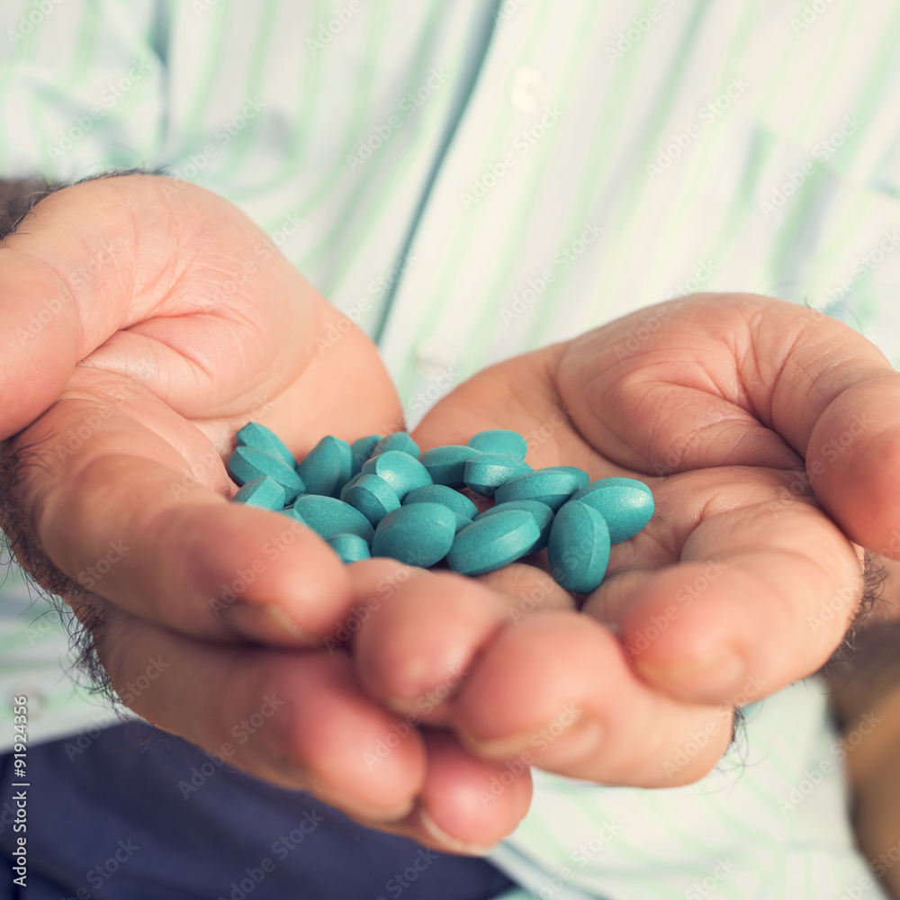 old man with a pile of blue pills in his hand old man with a pile of blue pills in his hand