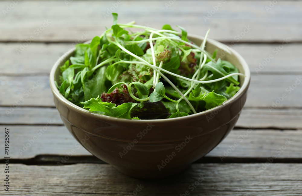 Fresh mixed green salad in bowl on wooden table close up Fresh mixed green salad in bowl on wooden table close up