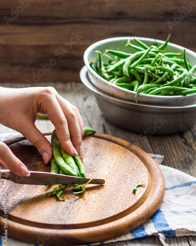 cut with a knife raw.green beans on a wooden board, hands