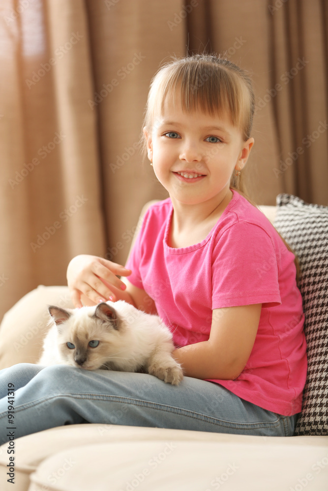 Obraz premium Little cute girl playing with kitten on sofa at home