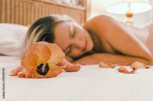 Maldivian flower on the bed in the bedroom on the background of a naked girl sleeping with her hair.