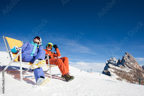 two snowboarders on top of the mountain having fun sitting on