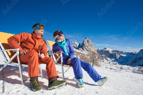 two snowboarders on top of the mountain having fun sitting on