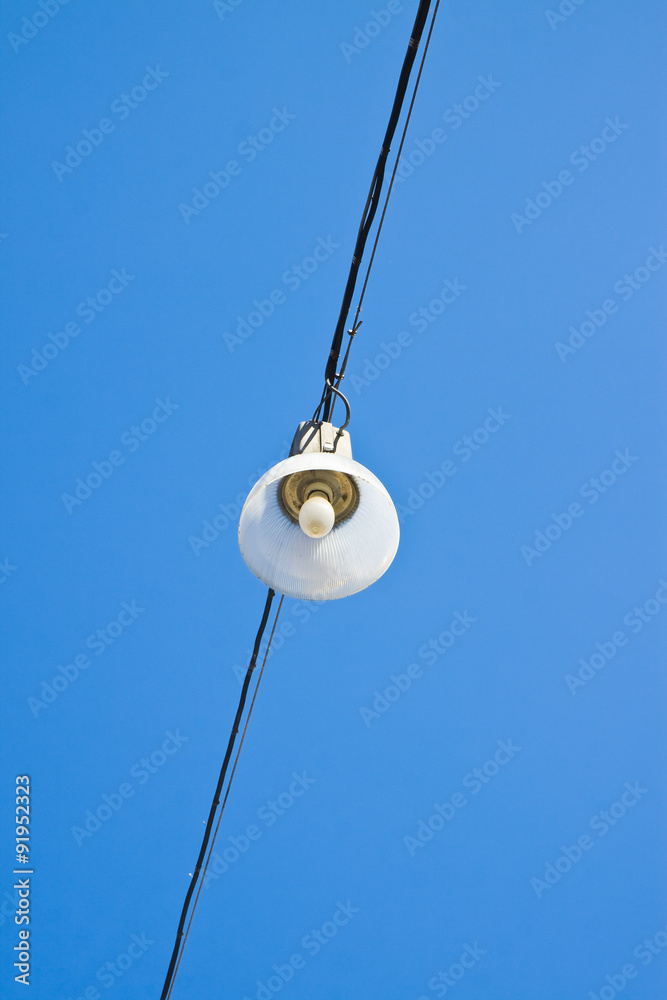 Single streetlight hanging from a metal cable on a blue background Single streetlight hanging from a metal cable on a blue background
