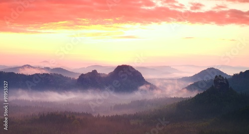 Red misty landscape panorama in mountains. Fantastic dreamy sunrise on rocky mountains. Foggy misty valley below
