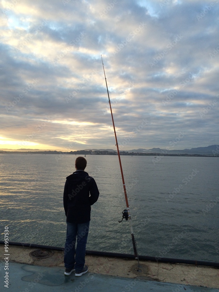 hombre joven pescando en el puerto al amanecer
