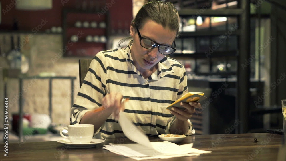 Sad, overwhelmed woman counting bills on smartphone in kitchen at home
Sad, overwhelmed woman counting bills on smartphone in kitchen at home