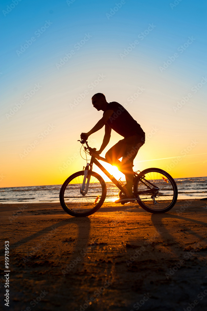 Naklejka premium Man cyclist silhouette on blue sky and multicolored sunset backg