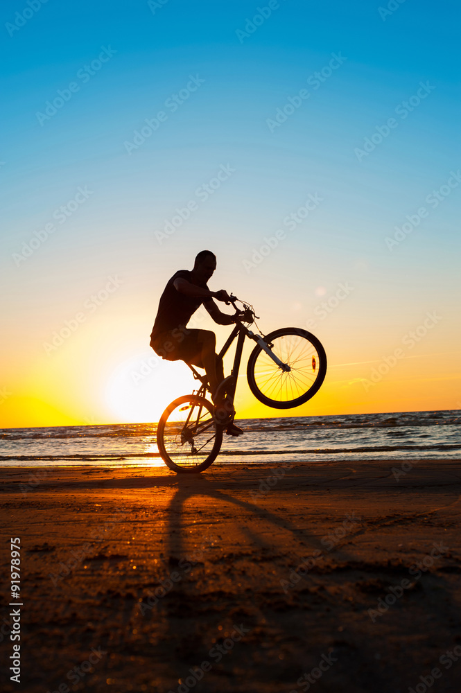 Obraz premium Man cyclist silhouette on blue sky and multicolored sunset backg