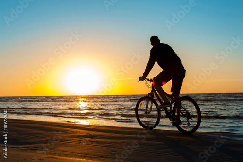 Man cyclist silhouette on blue sky and multicolored sunset backg