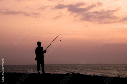 Silhouette of man fishing on the beach at seaside