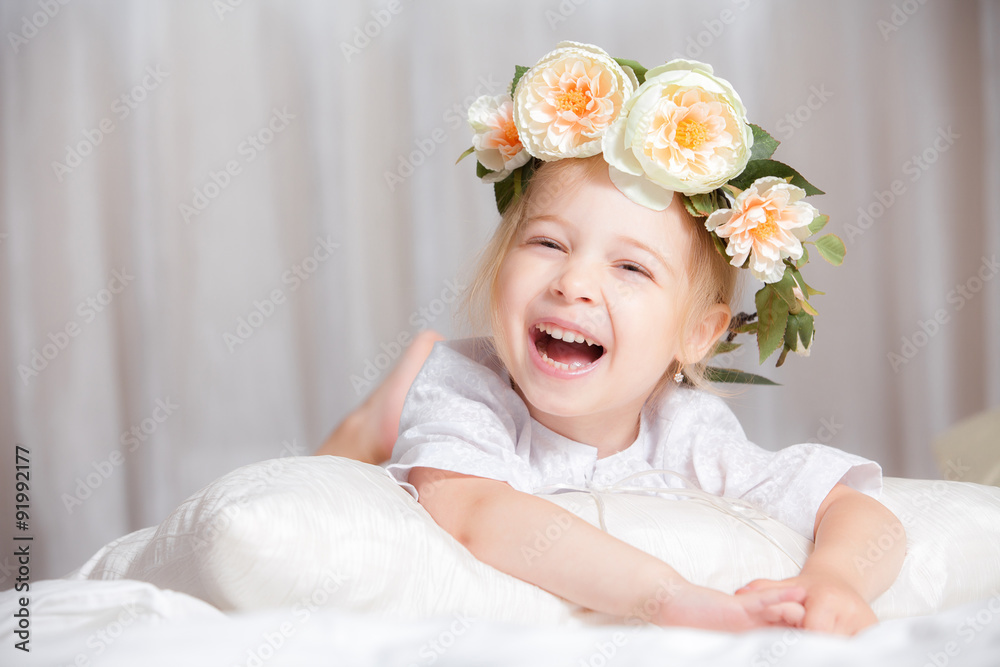 happy little girl with a wreath on the head on a bed happy little girl with a wreath on the head on a bed
