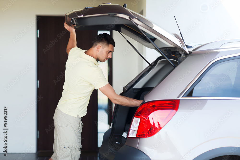 young man with open car trunk at parking space