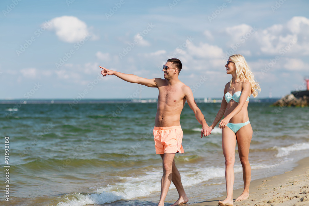 happy couple in swimwear walking on summer beach