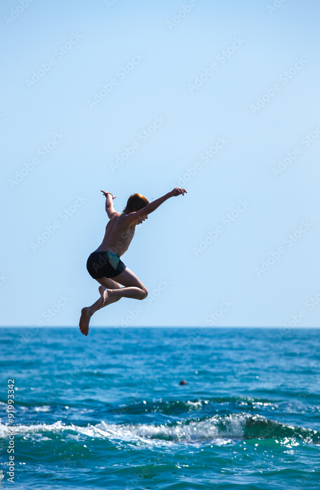 Boy jumping off cliff into the sea. Summer fun lifestyle