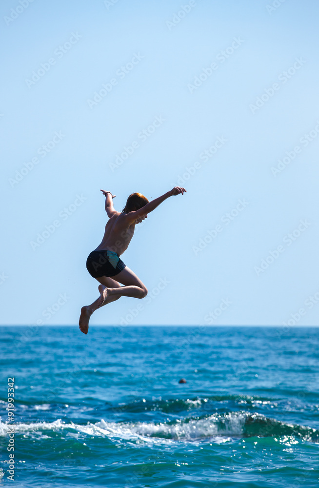 Boy jumping off cliff into the sea. Summer fun lifestyle Boy jumping off cliff into the sea. Summer fun lifestyle
