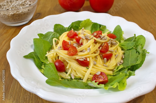 pasta with tomatoes, sunflower seeds and salad served on the wooden table