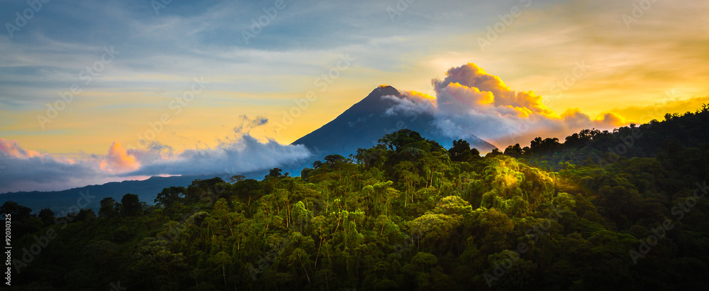 Obraz premium Wulkan Arenal o wschodzie słońca ... Rzadki widok w idealnym 15 sekundowym oknie, aby uchwycić wschód słońca w całej jego chwale. Światło lśni od chmur, góry i dżungli.