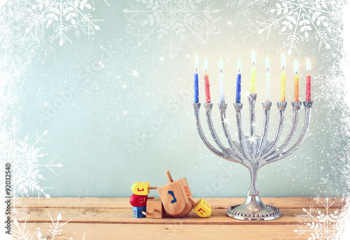 image of jewish holiday Hanukkah with menorah (traditional Candelabra) and wooden dreidels (spinning top). retro filtered image with glitter and snowflakes overlay
