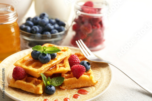 Sweet homemade waffles with forest berries and sauce on table background