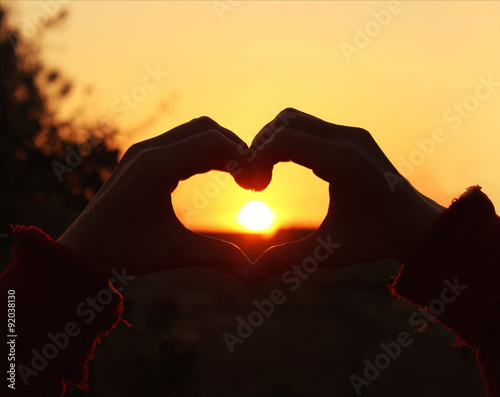 Women s hands are crossed in the form of the heart through which the sun s rays make the way at the sunset