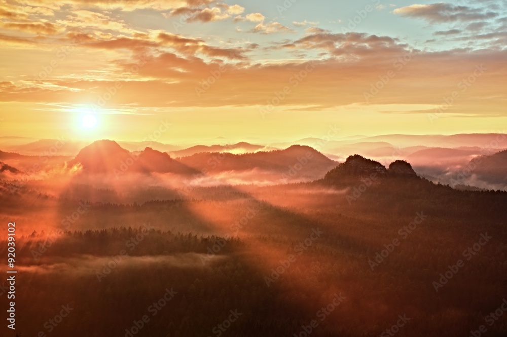 Red misty daybreak. Foggy autumn morning in a beautiful hills. Peaks of hills are sticking out from rich colorful clouds.