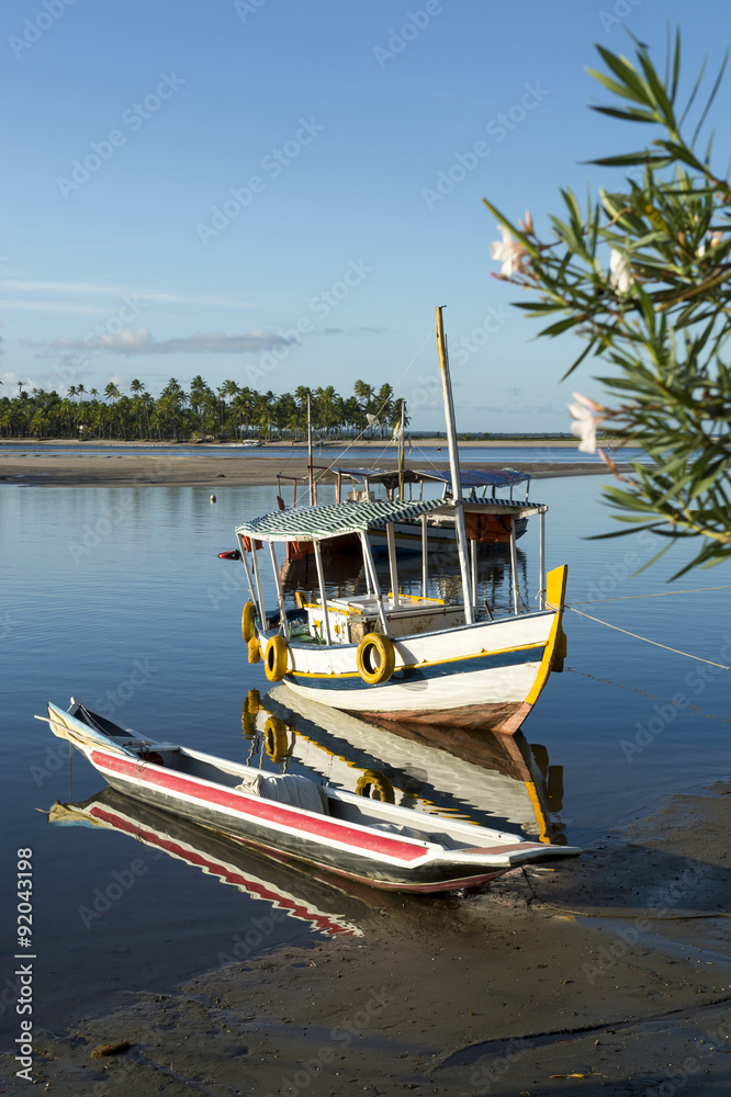 Colorful Brazilian fishing boat anchored next to canoe in shallow water off the coast of Bahia Nordeste Brazil