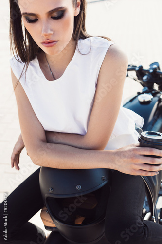 girl with cup of coffee sitting on vintage custom motorcycle