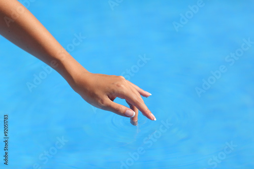 Beautiful woman hand touching blue water in a pool