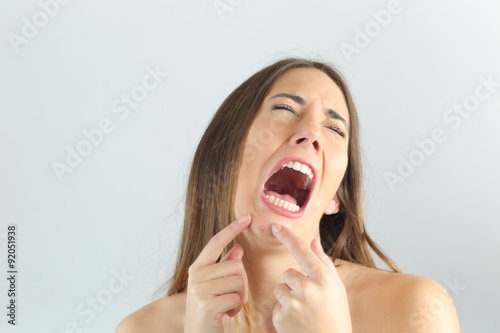 Girl crying while pressing a pimple on her chin