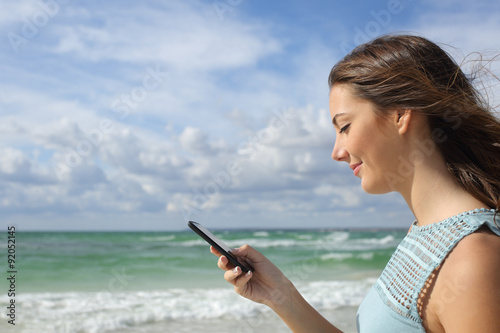 Profile of a girl using a smart phone on the beach