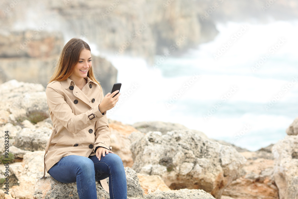 Woman using a smart phone in winter on the beach