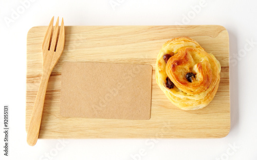 Raisin roll, note paper and fork on wooden tray