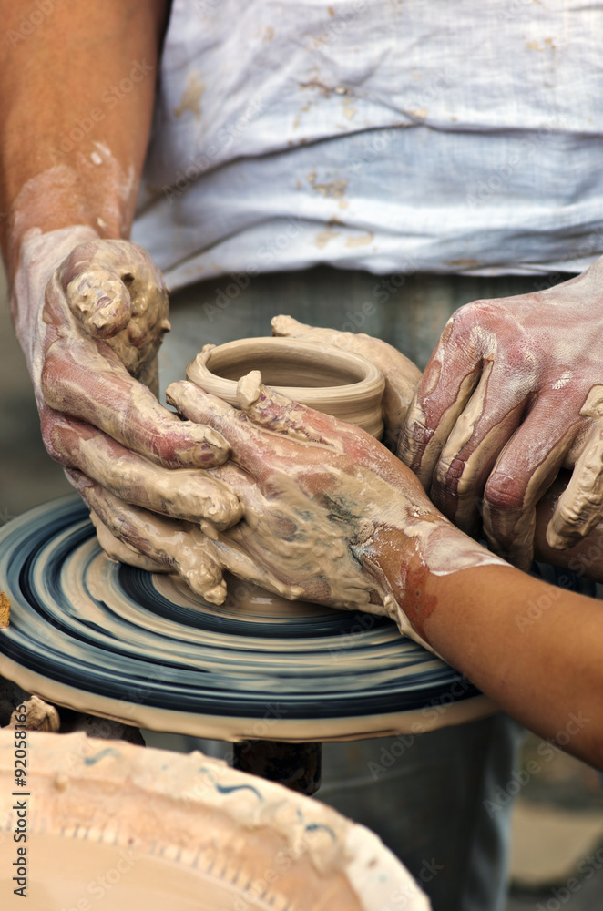 The hands of a potter help the child make a pitcher on a pottery