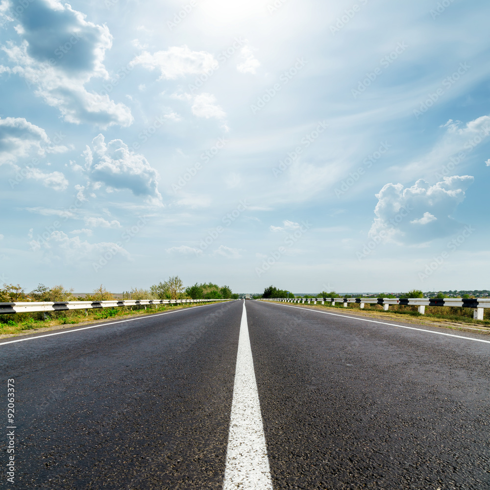 sun in dramatic sky over asphalt road