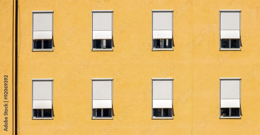 Obraz premium Wall in yellow colors with windows and shutters in high contrast