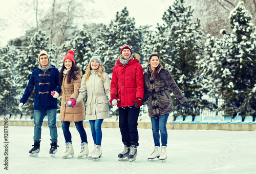 happy friends ice skating on rink outdoors