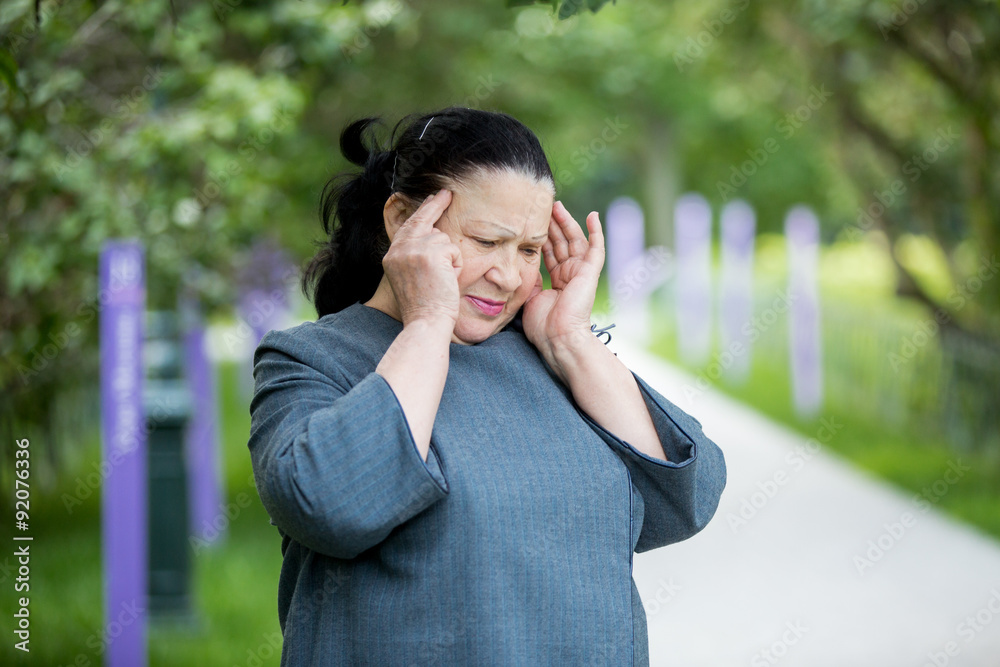 Mature woman with a headache standing in the park with her fingers to her temples. Her eyes closed, she is suffering.
Mature woman with a headache standing in the park with her fingers to her temples. Her eyes closed, she is suffering.