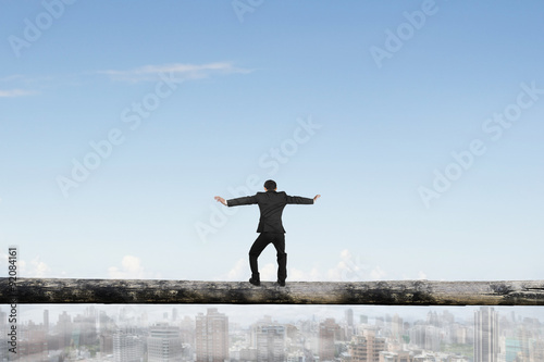 Rear view businessman balancing on tree trunk high in sky