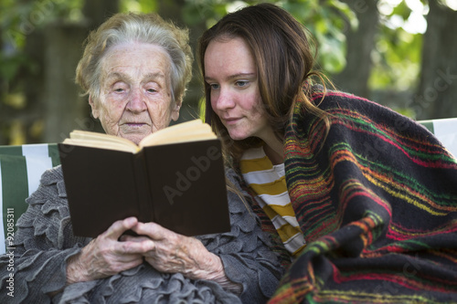 Grandmother and granddaughter reading a book while sitting in the Park.
