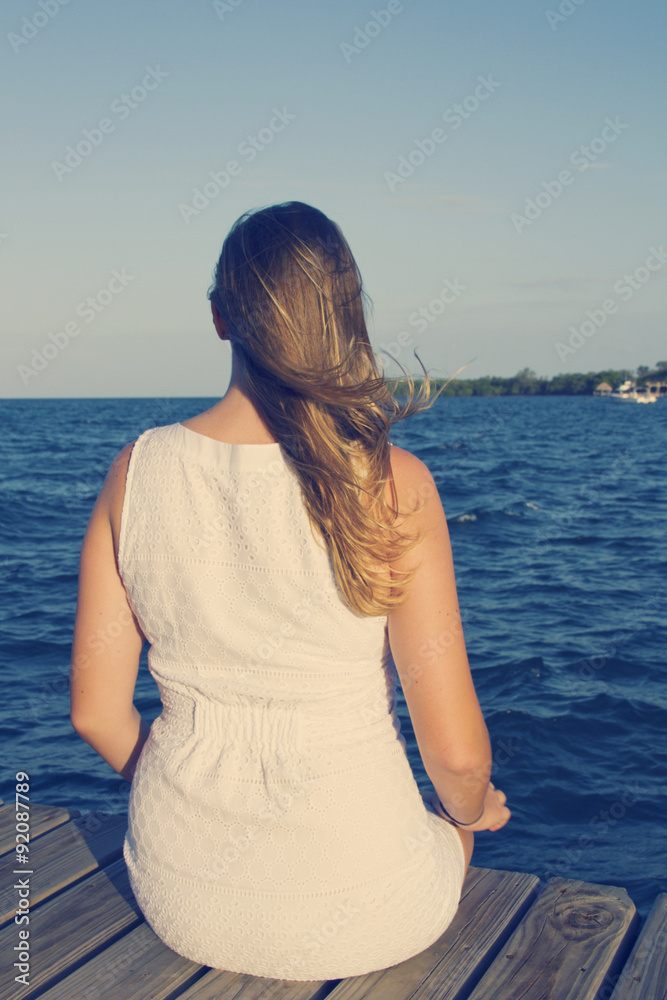 Fototapeta premium Woman sitting on dock, looking toward ocean