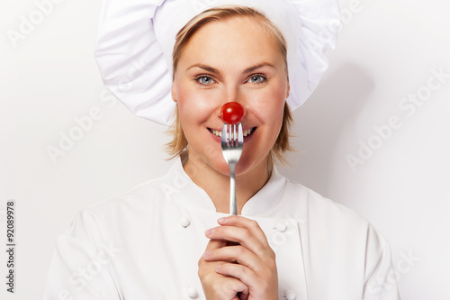 Chef woman holdinh a fork with tomato against her nose, standing photo